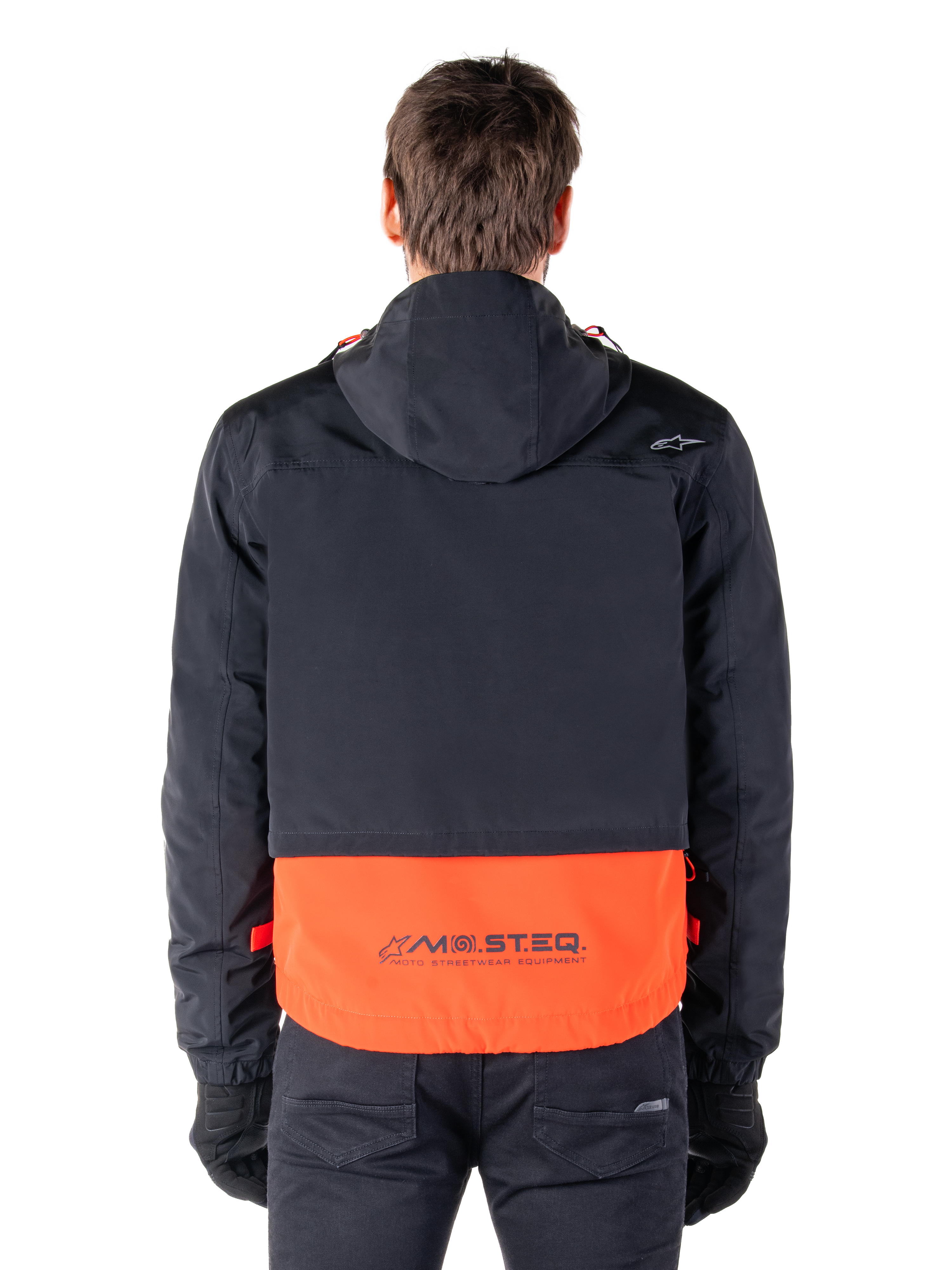 Alpinestars Mootant vandtæt parka i Spicy Orange og sort, set bagfra, viser sort overdel med hætte og orange underpanel med MO.ST.EQ.-ordmærket, funktionelt motorcykel-streetwear.
