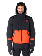 Alpinestars Mootant vandtæt parka, motorcykeljakke, Spicy Orange og sort, modulært helårsdesign med hætte, lynlåslommer foran og orange stropdetaljer på ærmerne, båret af en model med sorte handsker og bukser