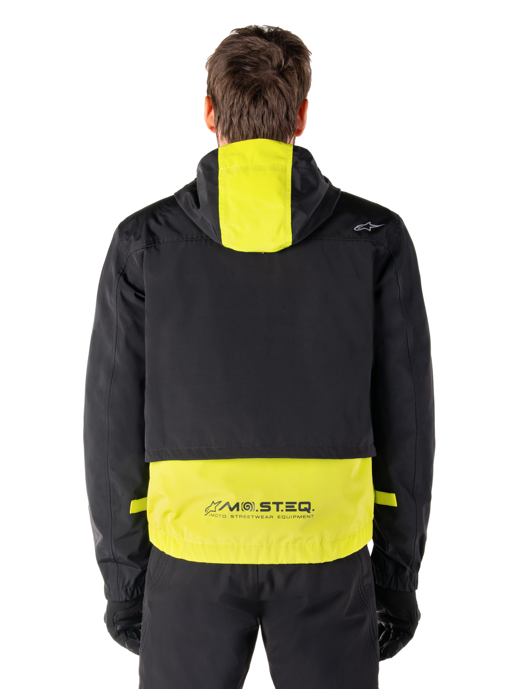 Alpinestars Mootant vandtæt parka, motorcykeljakke, Lime Punch og sort, set bagfra der viser designet med hætte og reflekterende MO.ST.EQ.-branding på den nederste del af ryggen, båret med sorte kørebukser og handsker.