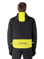 Alpinestars Mootant vandtæt parka, motorcykeljakke, Lime Punch og sort, set bagfra der viser designet med hætte og reflekterende MO.ST.EQ.-branding på den nederste del af ryggen, båret med sorte kørebukser og handsker.