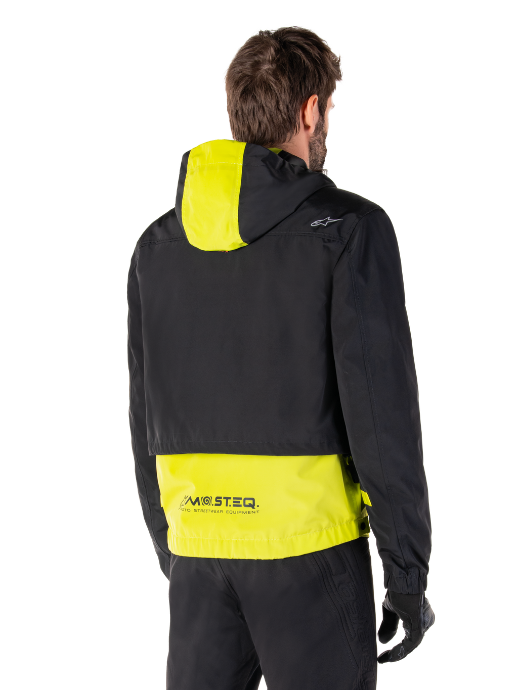 Alpinestars Mootant vandtæt parka, set bagfra, Lime Punch og sort, med sort overdel, limegult panel på hætten og den nederste del af ryggen, MO.ST.EQ.-branding på kanten, båret med sorte motorcykelbukser og handsker, moderne urban motorcykeljakke
