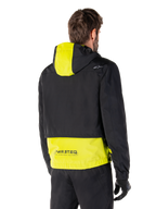 Alpinestars Mootant vandtæt parka, set bagfra, Lime Punch og sort, med sort overdel, limegult panel på hætten og den nederste del af ryggen, MO.ST.EQ.-branding på kanten, båret med sorte motorcykelbukser og handsker, moderne urban motorcykeljakke