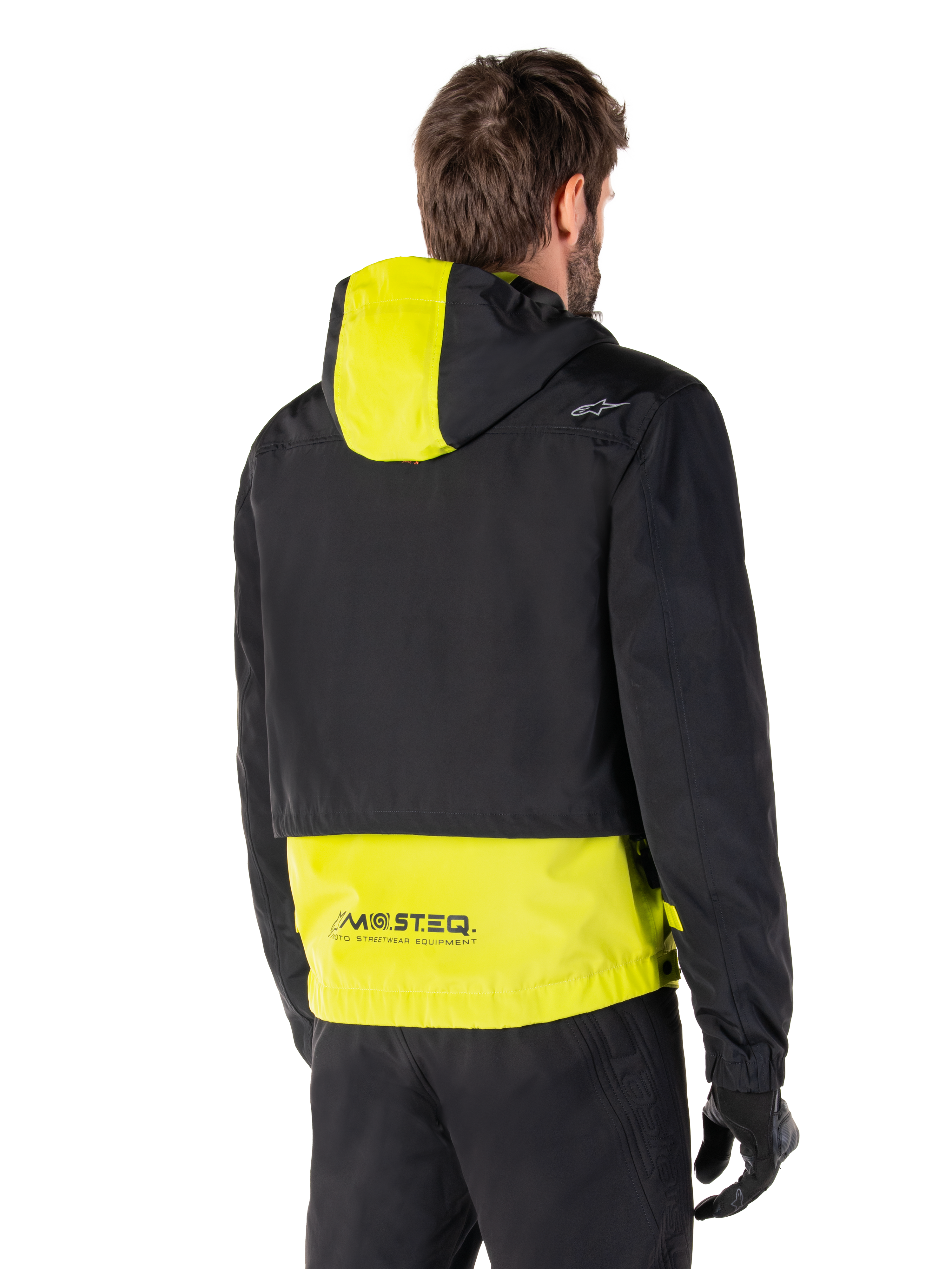 Alpinestars Mootant vandtæt parka, set bagfra, Lime Punch og sort, med sort overdel, limegult panel på hætten og den nederste del af ryggen, MO.ST.EQ.-branding på kanten, båret med sorte motorcykelbukser og handsker, moderne urban motorcykeljakke