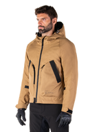 Alpinestars Morush Vandtæt Parka, Utility Brown, mandlig model iført parka med sorte kørehandsker og sorte bukser, minimalistisk streetwear-inspireret design med stormsikker hætte og store forlommer, vandtæt motorcykelbeklædning