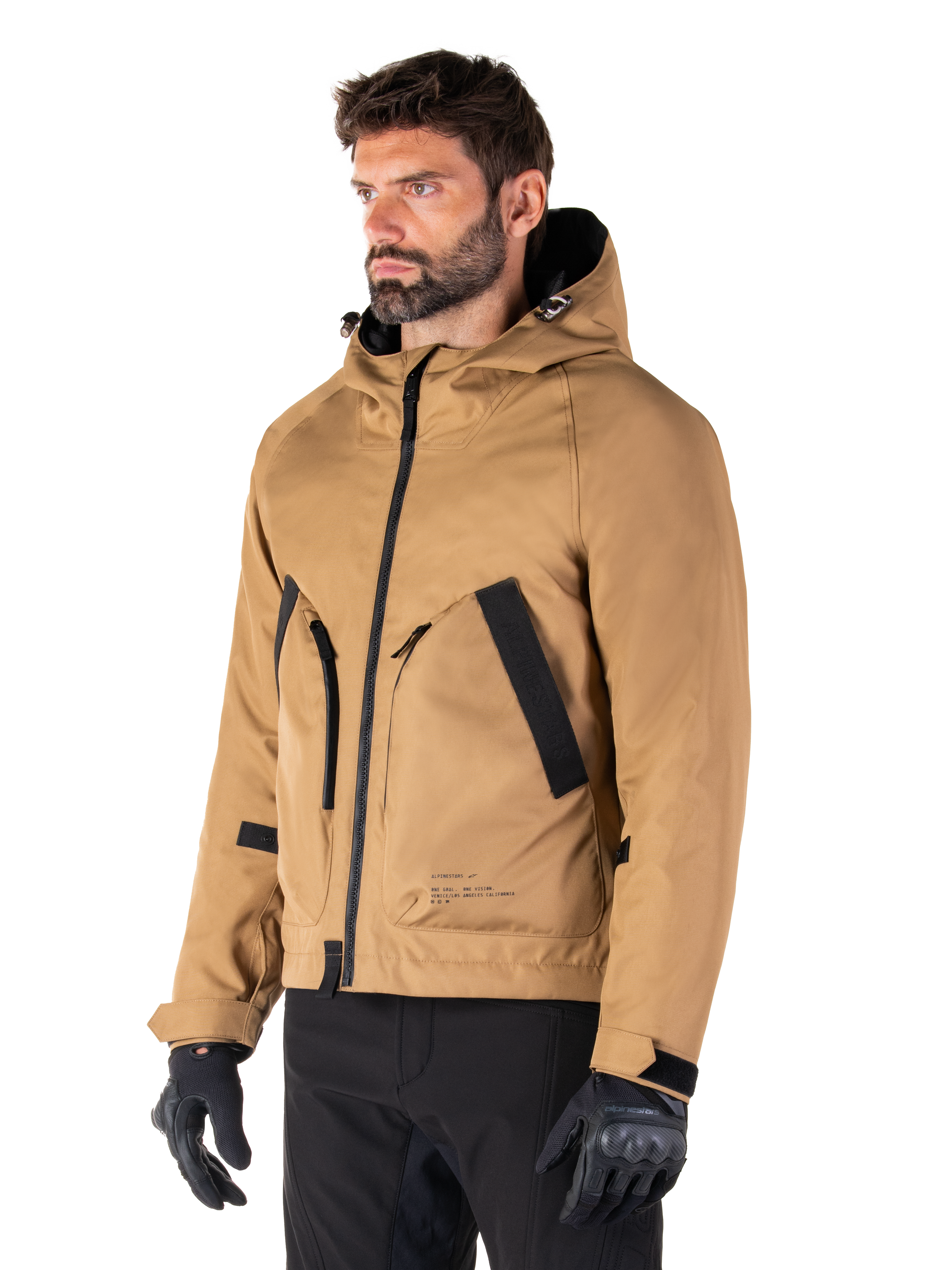 Alpinestars Morush Vandtæt Parka, Utility Brown, mandlig model iført parka med sorte kørehandsker og sorte bukser, minimalistisk streetwear-inspireret design med stormsikker hætte og store forlommer, vandtæt motorcykelbeklædning