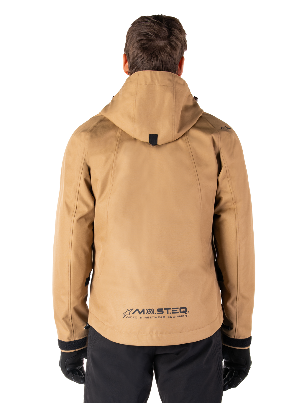 Alpinestars Morush vandtæt parka, Utility Brown, set bagfra, med hætte og MO.ST.EQ.-branding nederst på ryggen, kombineret med sorte bukser og handsker, moderne streetwear-inspireret motorcykeludstyr