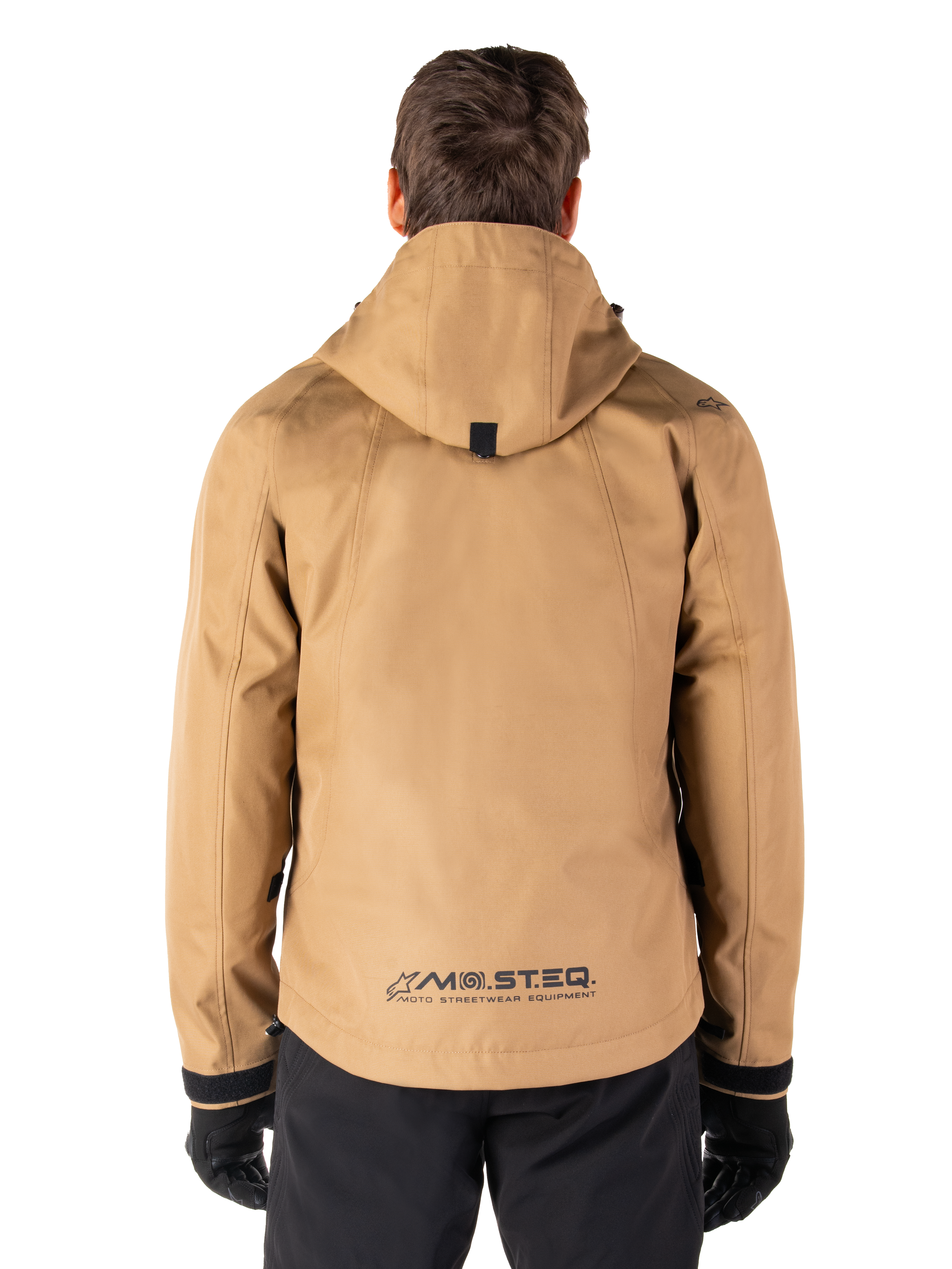 Alpinestars Morush vandtæt parka, Utility Brown, set bagfra, med hætte og MO.ST.EQ.-branding nederst på ryggen, kombineret med sorte bukser og handsker, moderne streetwear-inspireret motorcykeludstyr