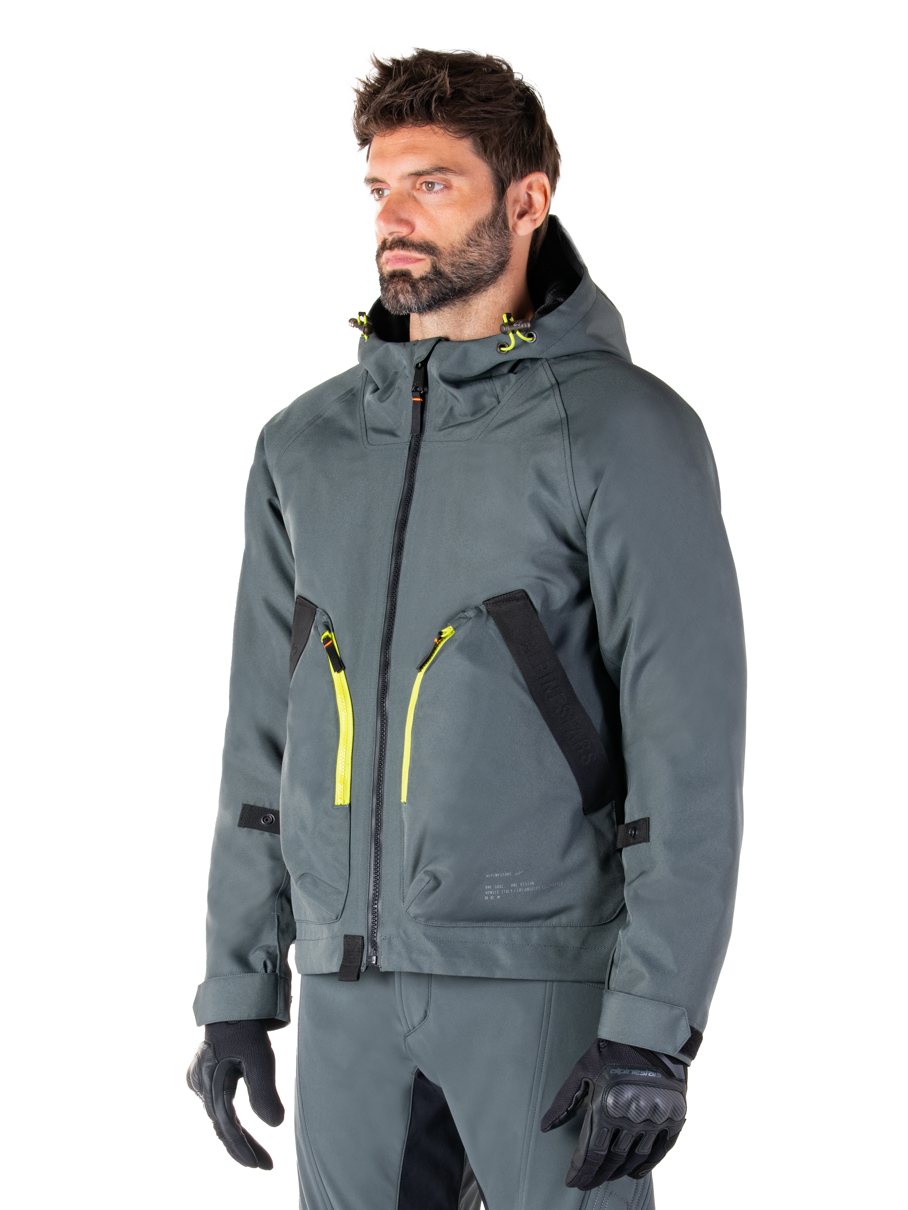 Alpinestars Morush Waterproof Parka, Urban Gray motorcykeljakke, design med hætte og klare gule lynlåsdetaljer, sorte lommedetaljer, båret med matchende grå kørebukser og sorte handsker, moderne streetwear-inspireret motorcykelbeklædning.