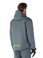 Alpinestars Morush Vandtæt Parka i Urban Gray, set bagfra, med gul MO.ST.EQ.-branding på lænden og skulderen, minimalistisk design med hætte, bæres med matchende grå kørebukser og sorte handsker, urban motorcykel-streetwear
