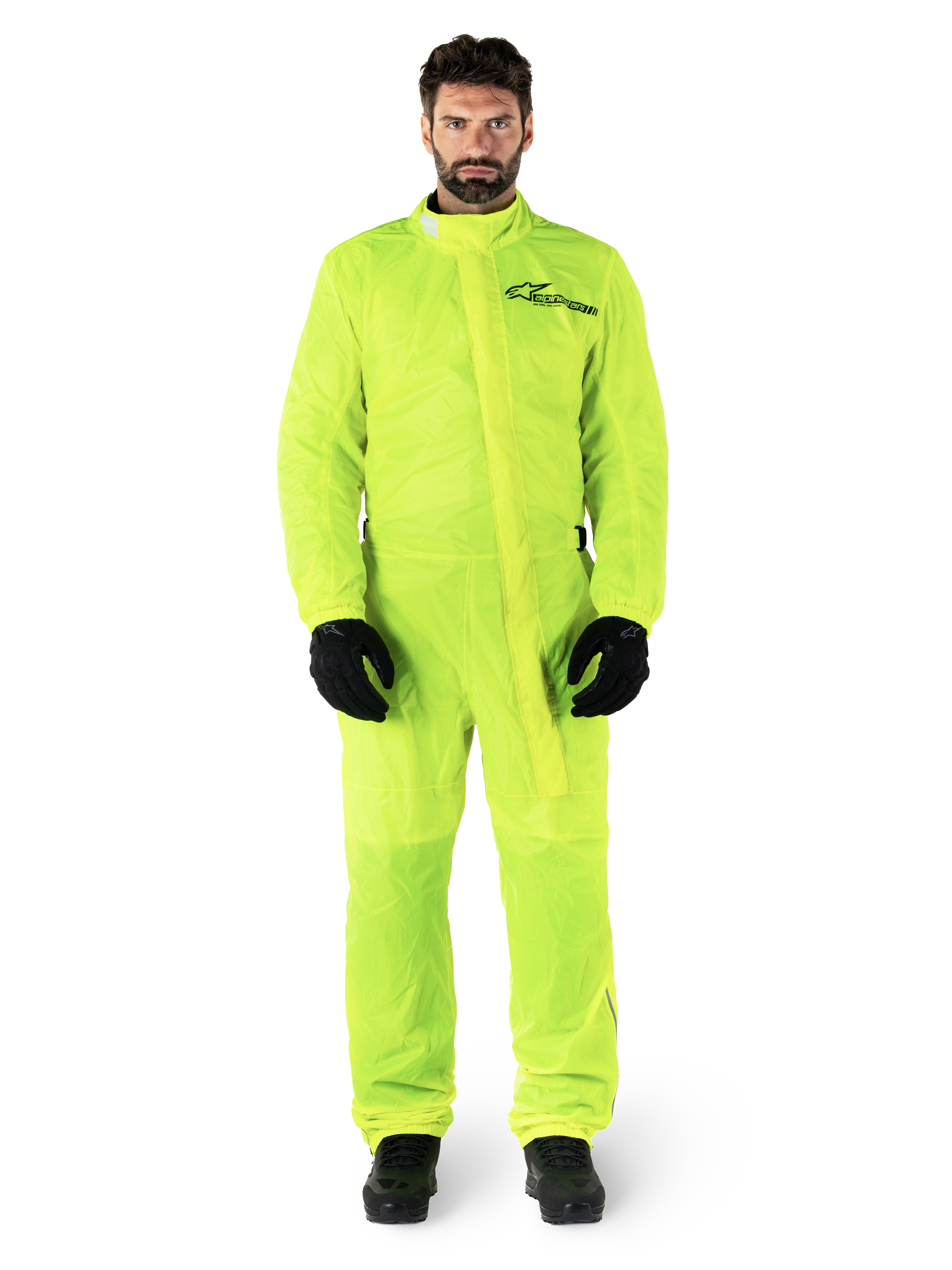 Alpinestars Hurricane Rain V2-dragt, motorcykelregndragt, neongul, mandlig model iført fuldkropsbeskyttelse med sorte handsker og støvler, høj krave med stormflap foran, reflekterende logo på brystet, vandtæt udstyr med høj synlighed