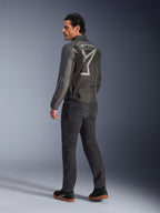 Alpinestars Axton-jakke, motorcykeljakke til mænd, sort og antracit, set bagfra med et stort gråt kropsomsluttende logo og akkordeon-skulderpaneler, båret med mørke kørebukser og sorte sneakers, urban moderne stil med racing-arv.