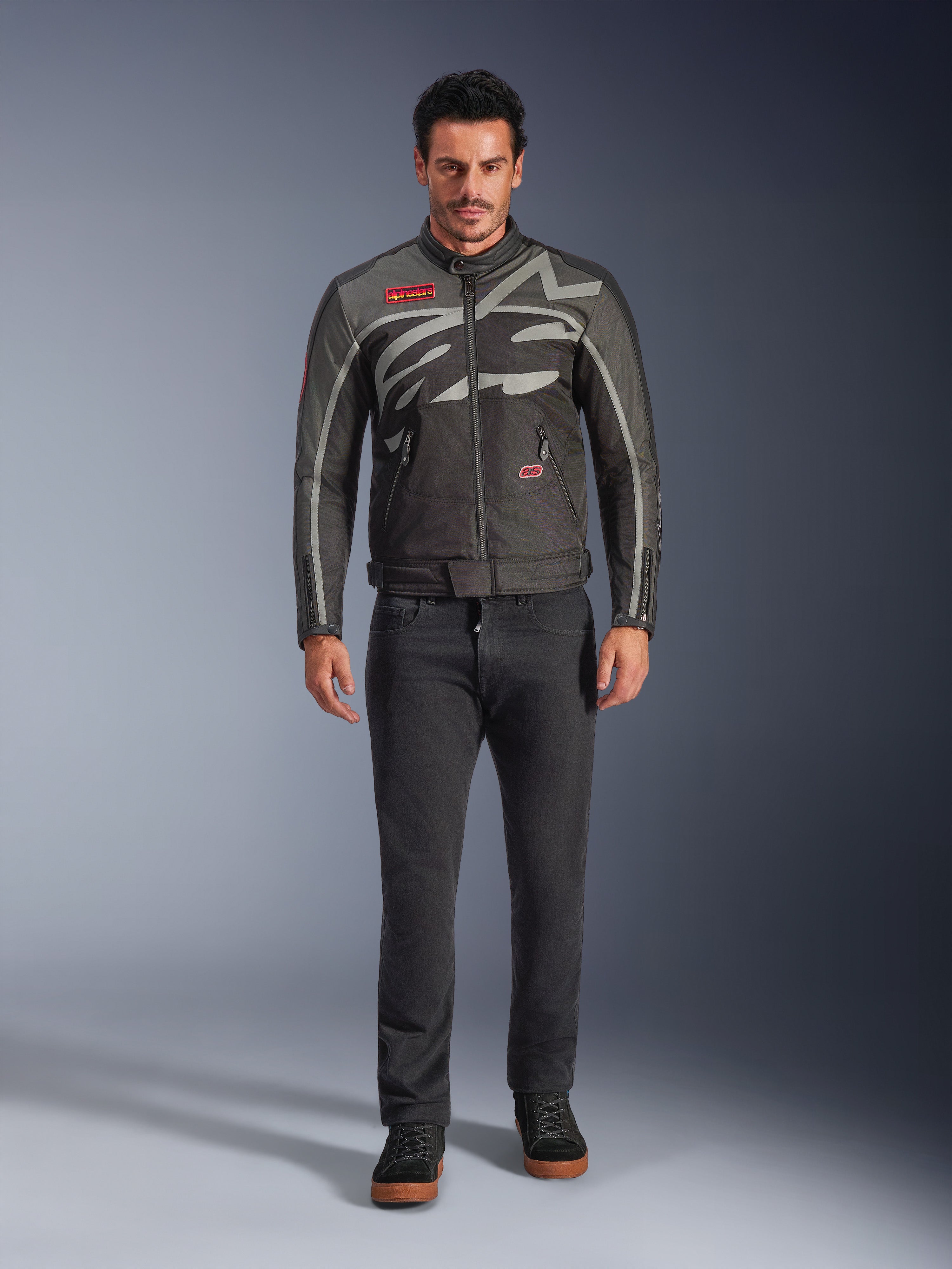 Alpinestars Axton-jakke, motorcykeljakke, sort, antracitgrå, rød og tangerine, båret af en model med mørke bukser, kropsomsluttende gråt Alpinestars-logo, røde mærkepatches, vandafvisende tekstilskal til bykørsel