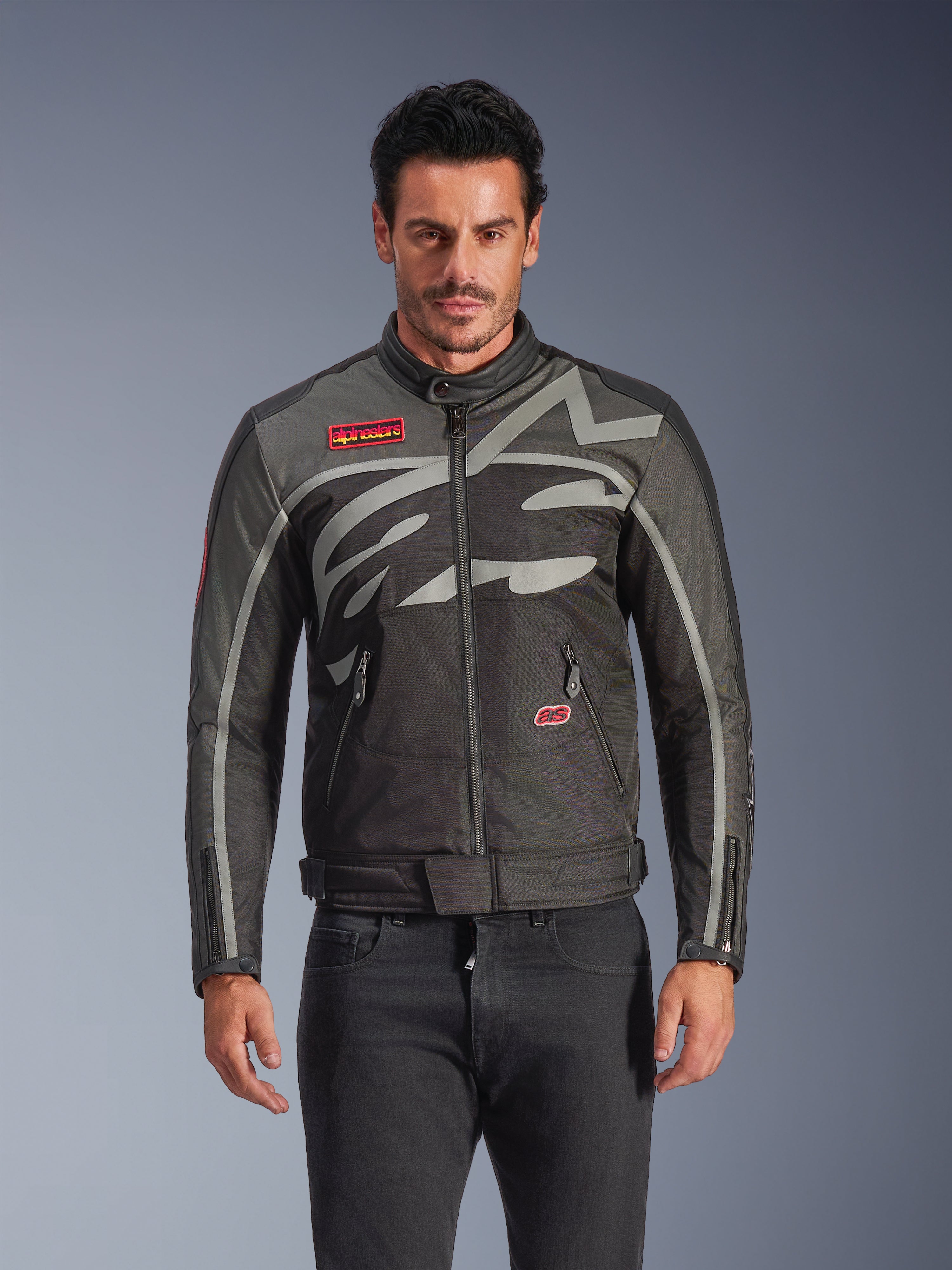 Alpinestars Axton jakke, urban motorcykeljakke til mænd, sort og antracit med røde detaljer, stor omsluttende lysegrå grafik, røde patches på brystet og lommen, lynlås foran og ved manchetterne, vintage-inspireret racing-design til bykørsel