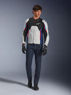 Mandlig model iført Alpinestars AST V3 Air-jakke i Silver Deep Blue Bright Red, med mesh-ventilation og perforerede paneler, kombineret med mørkeblå denim motorcykeljeans og sorte handsker, sportsoptimeret udstyr til varmt vejr.