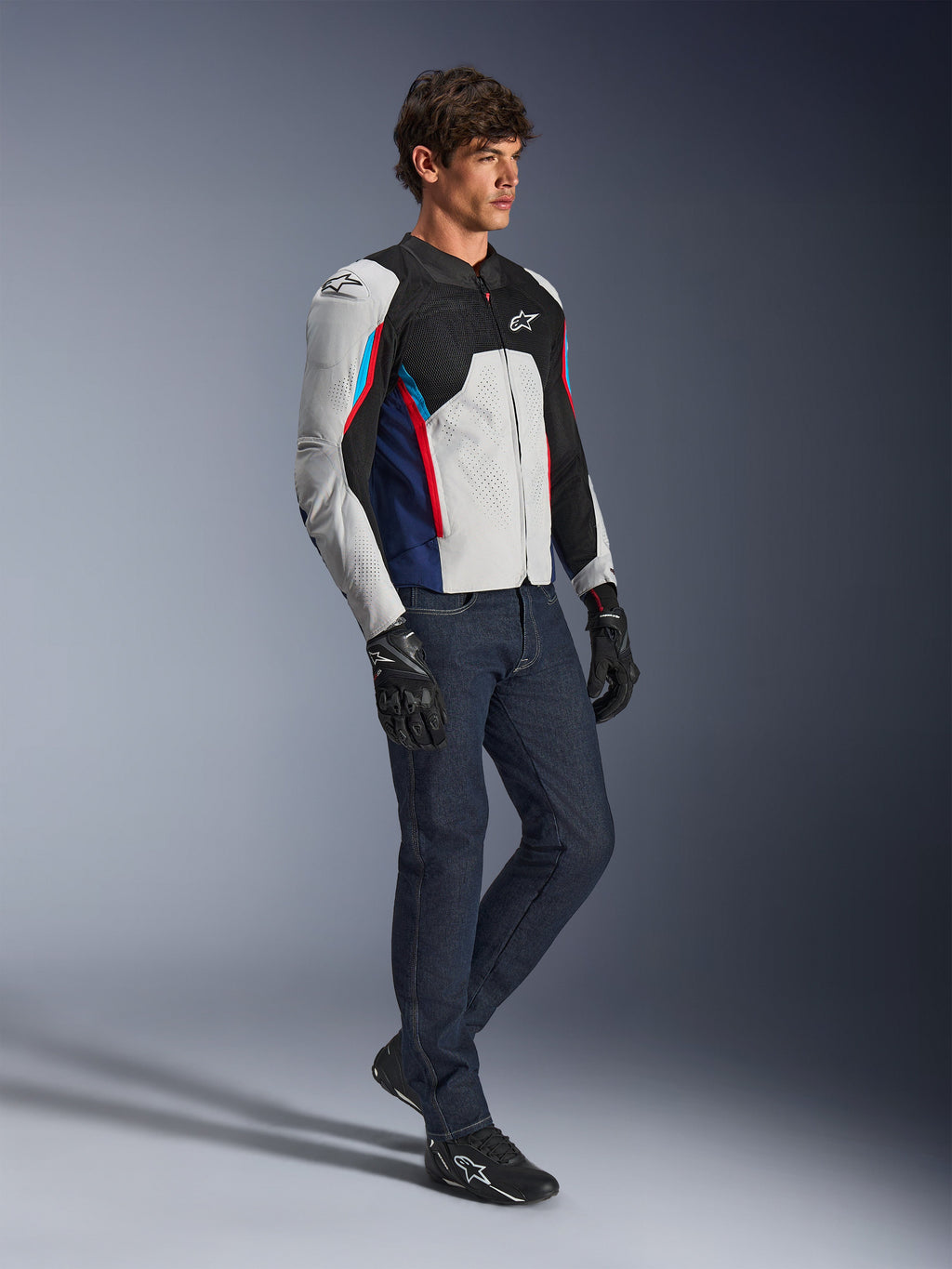 Alpinestars AST V3 Air Jakke, motorcykeljakke, sølv, mørkeblå og klar rød, båret med mørke denimjeans og sorte kørehandsker, med ventilerede mesh-paneler og et sport-fit design til kørsel i varmt vejr