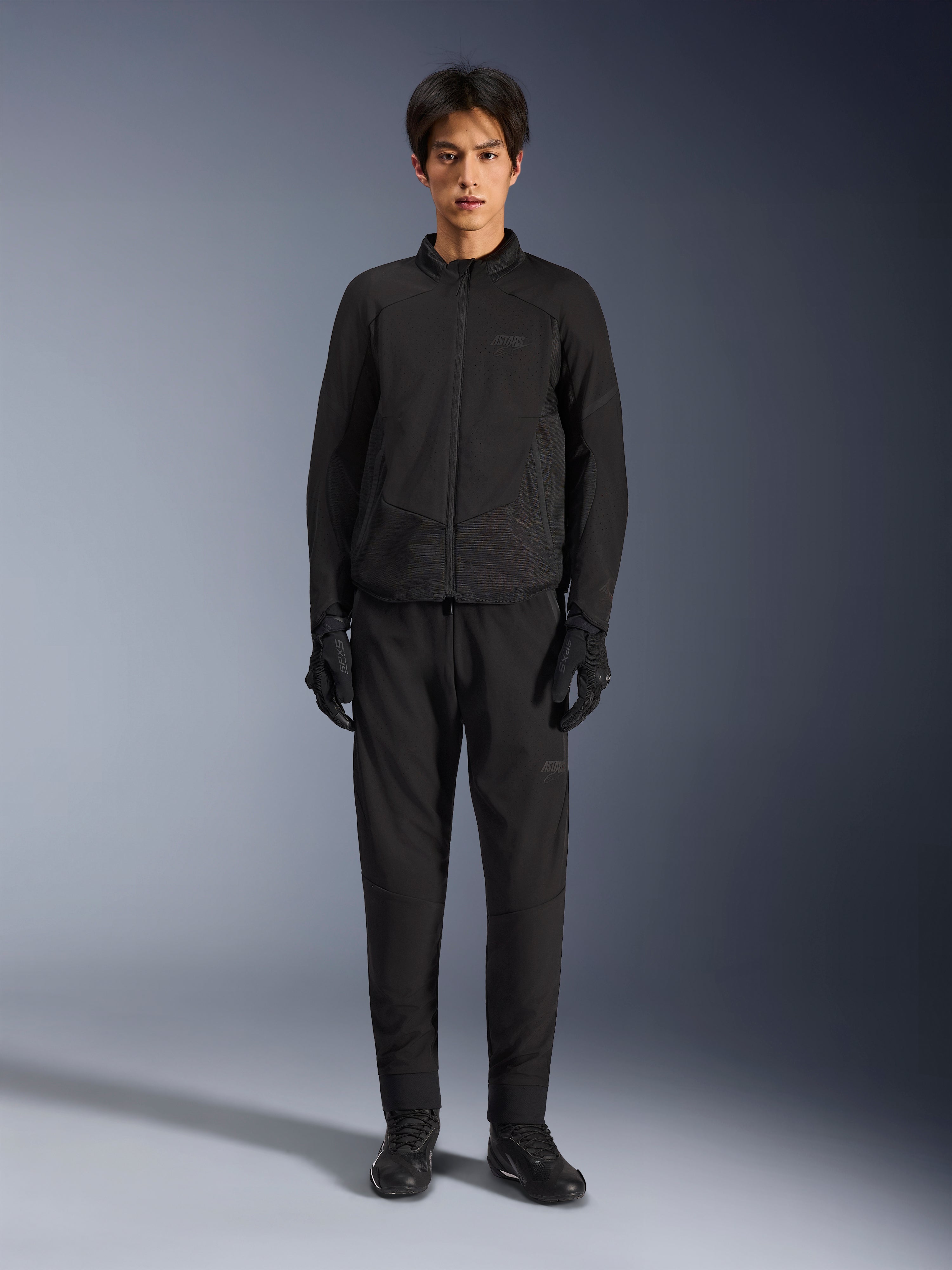 Alpinestars Aeroshell Airflow Jakke, sort motorcykeljakke, båret af model med matchende sorte bukser og handsker, med laserperforerede bryst- og sidemesh-paneler, sport-cut pasform til ydeevne i varmt vejr