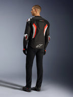 Alpinestars T-GP Air-jakke, Black Red Fluo motorcykeljakke, set bagfra på en model, med ventilationspaneler i mesh, aerodynamisk pukkel og hvide udvendige beskyttere på albuer og skuldre, båret med sorte bukser og køresko