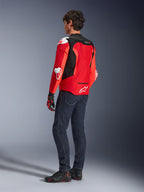 Alpinestars T-GP Air Jacket, Rear view of a man wearing a bright red and fluo red textile jacket with black mesh panels and white armor sliders, paired with dark blue jeans and black riding shoes, sport motorcycle riding gear.