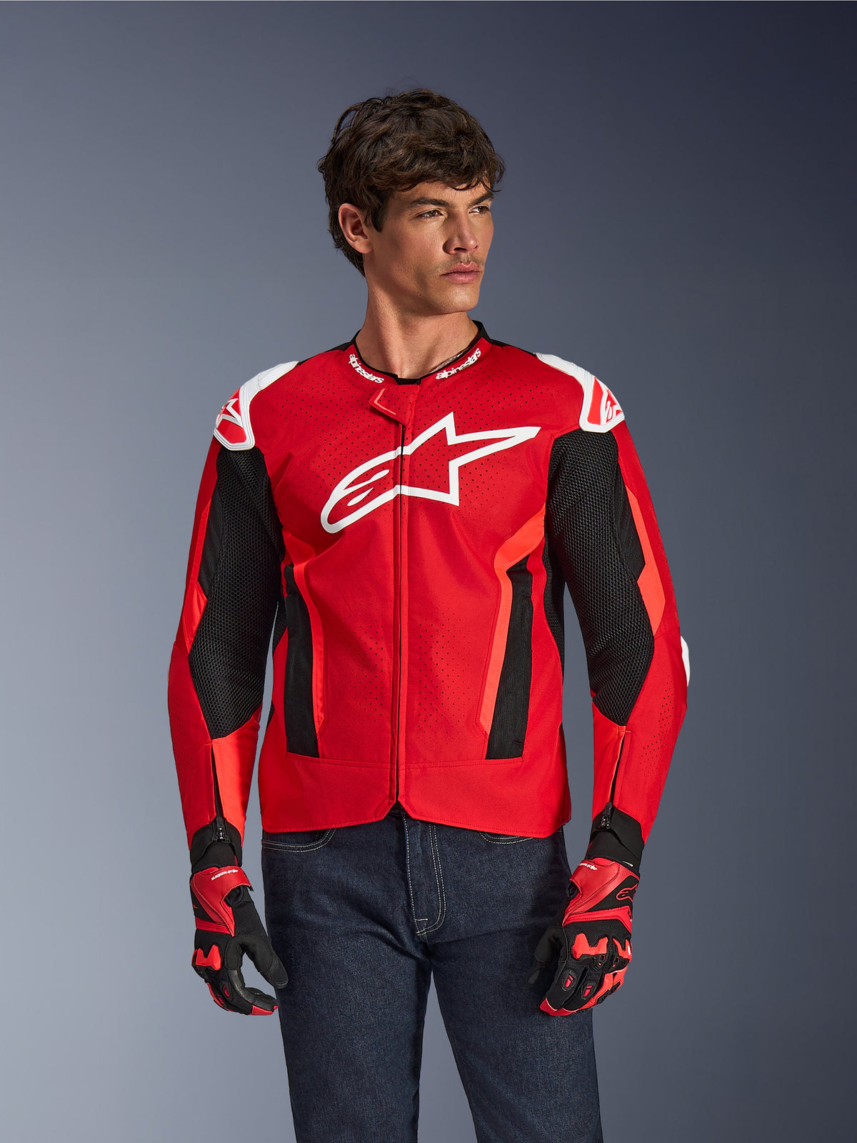 Alpinestars T-GP Air jakke, motorcykeljakke, klar rød og sort med hvidt logo, med perforerede mesh-ventilationspaneler, båret med matchende handsker og mørke denimjeans, sporty design til kørsel i varmt vejr