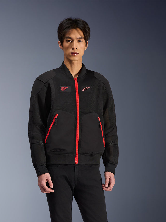 Alpinestars Flight Air-jakke i sort og klar rød, urban motorcykeljakke i bomber-stil båret af en model, med ventilationspaneler i mesh, en markant rød frontlynlås, røde lommedetaljer og branding på brystet, stylet med sorte bukser