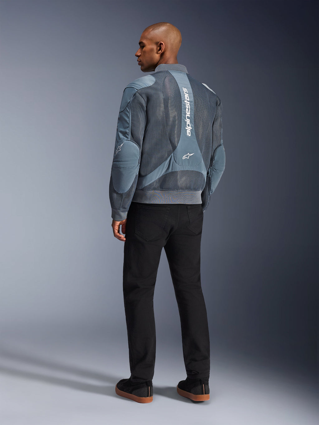 Alpinestars Flight Air Jacket, Storm Gray motorcycle jacket, back view, featuring 3D mesh ventilation panels and vertical white Alpinestars branding, worn with black pants and black sneakers, urban commuter style