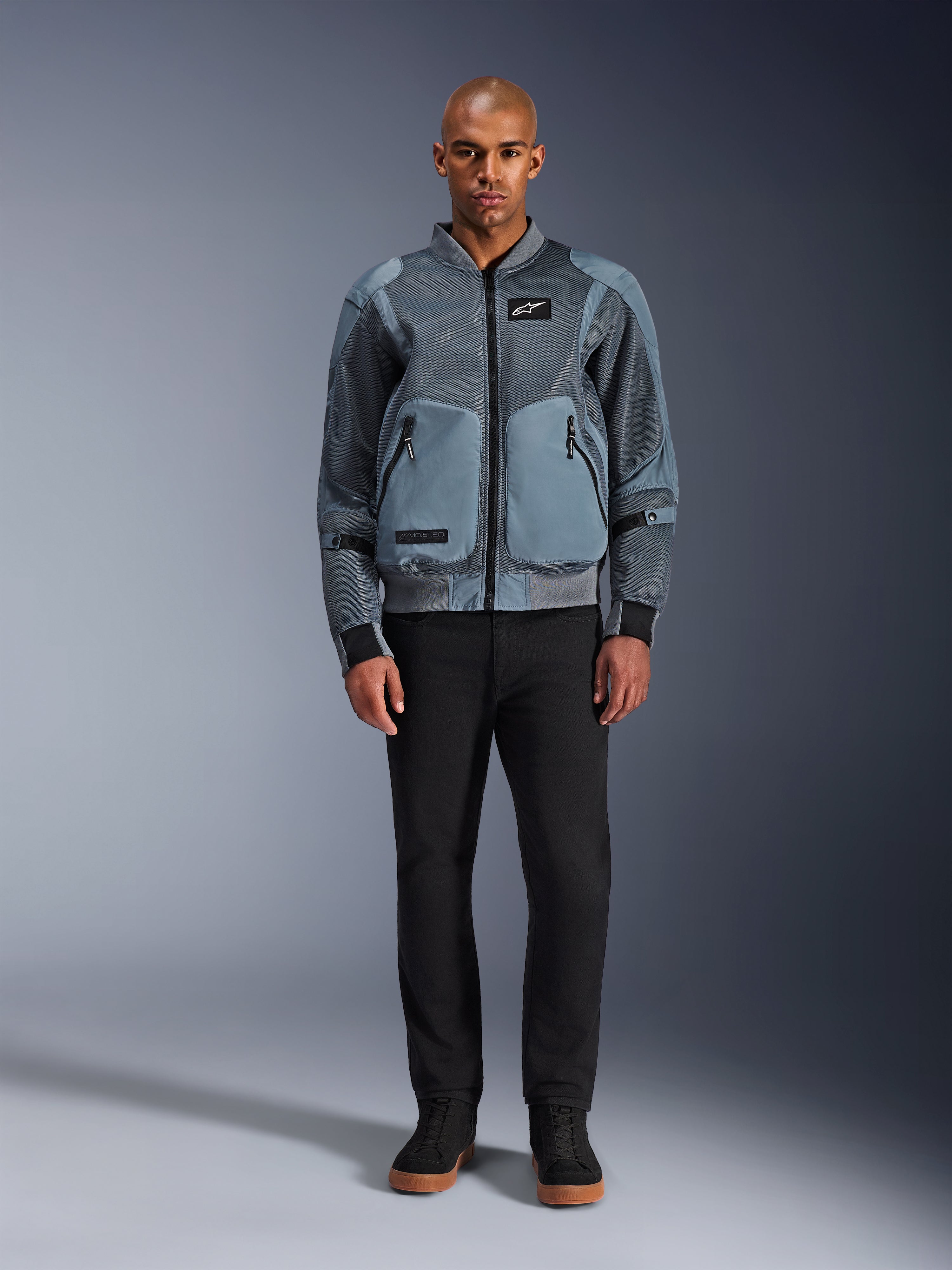 Alpinestars Flight Air Jacket in Storm Gray, urban bomber-inspired motorcycle jacket featuring 3D mesh panels and solid front pockets, worn by a man with black pants and black high-top sneakers, modern street-style riding apparel