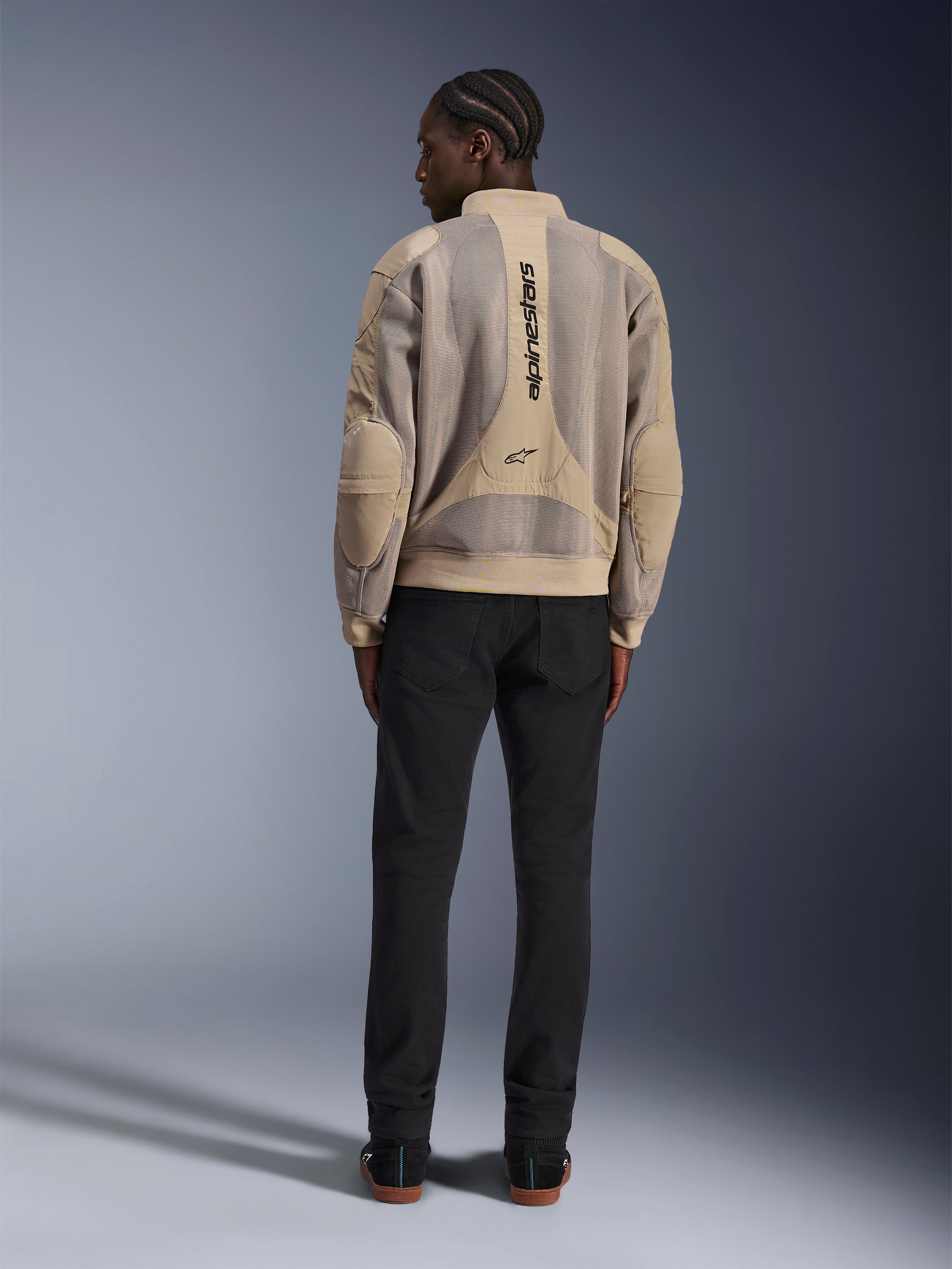 Alpinestars Flight Air-jakke, tan urban motorcykeljakke, set bagfra, viser åndbare 3D-mesh-paneler og lodret logo, båret med sorte bukser for et moderne streetstyle-look