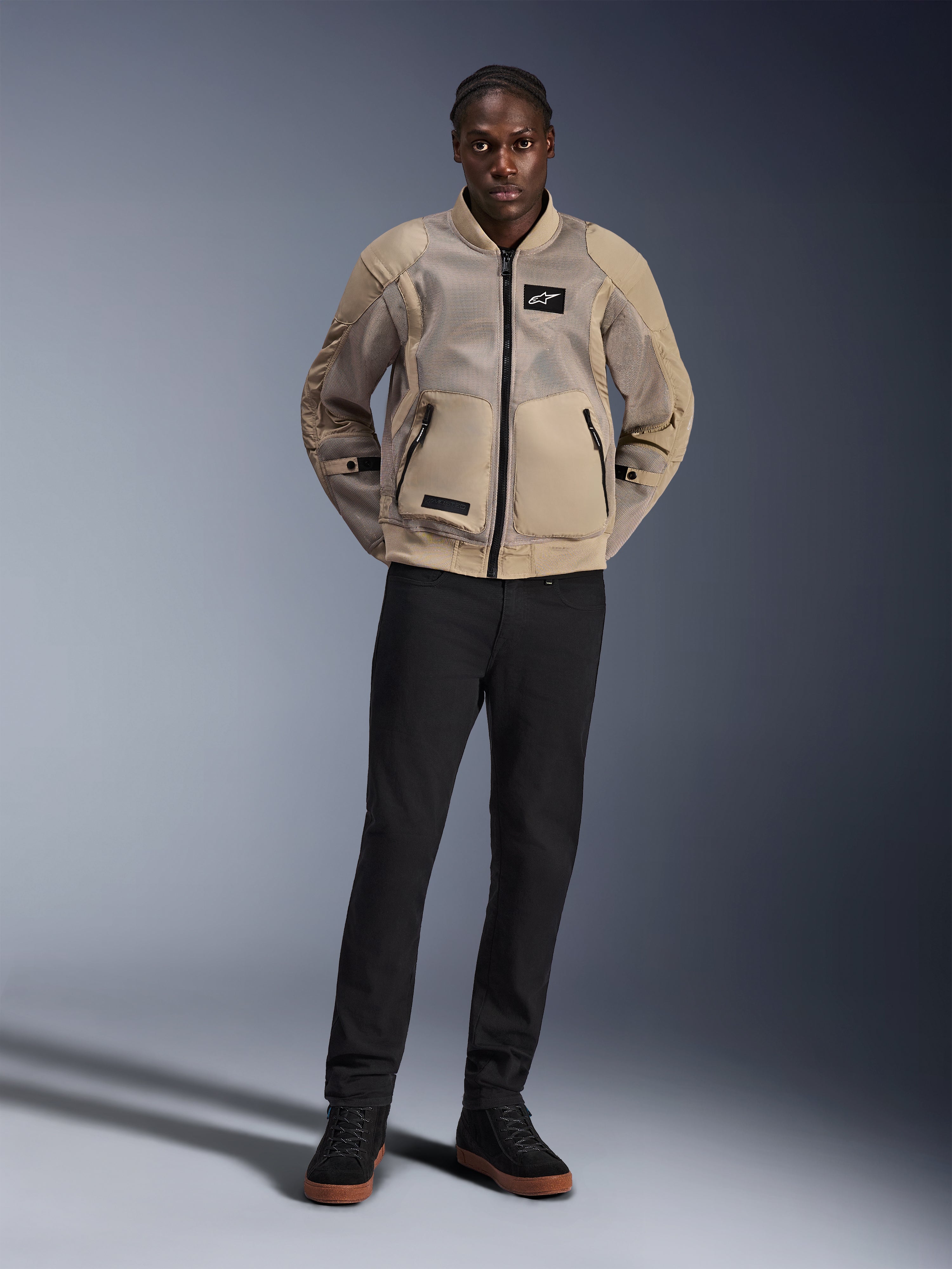 Model iført Alpinestars Flight Air Jacket i brun, urban motorcykeljakke med udvidede 3D mesh-paneler, bomber-inspireret ribstrikket krave og manchetter, stylet med sorte bukser og sorte køresko, moderne street-ready udstyr
