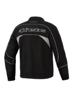 Alpinestars Unite-jakke, set bagfra, sort med mørkegrå reflekterende paneler, Alpinestars-branding med hvidt omrids på tværs af ryggen, urban motorcykel-softshelljakke med minimalistisk design