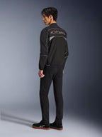Alpinestars Unite jakke, urban motorcykeljakke, sort og mørkegrå, set bagfra med stort kontureret Alpinestars-logo, reflekterende piping og paneler, minimalistisk softshell-design, båret med sorte bukser og afslappet fodtøj