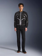 Alpinestars Unite-jakke, motorcykeljakke, sort og mørkegrå, båret af en model med sorte bukser og sorte støvler, med hvide kontrastlynlåse, reflekterende piping og minimalistisk urbant design