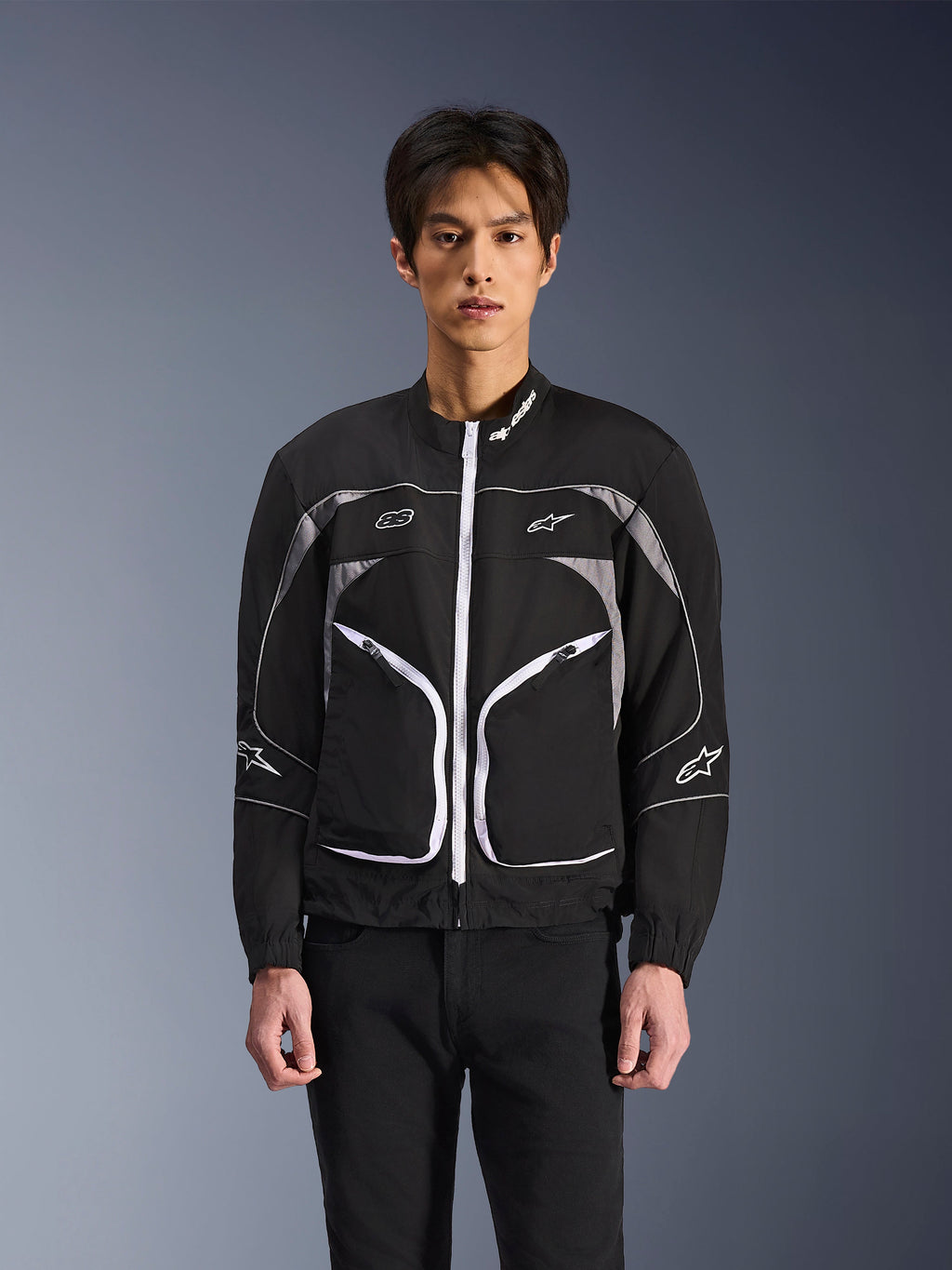 Alpinestars Unite-jakke, minimalistisk urban motorcykeljakke, sort og mørkegrå med hvide detaljer, hvid lynlås foran, reflekterende piping og Alpinestars-branding på brystet og ærmerne, moderne streetwear-stil til kørere.