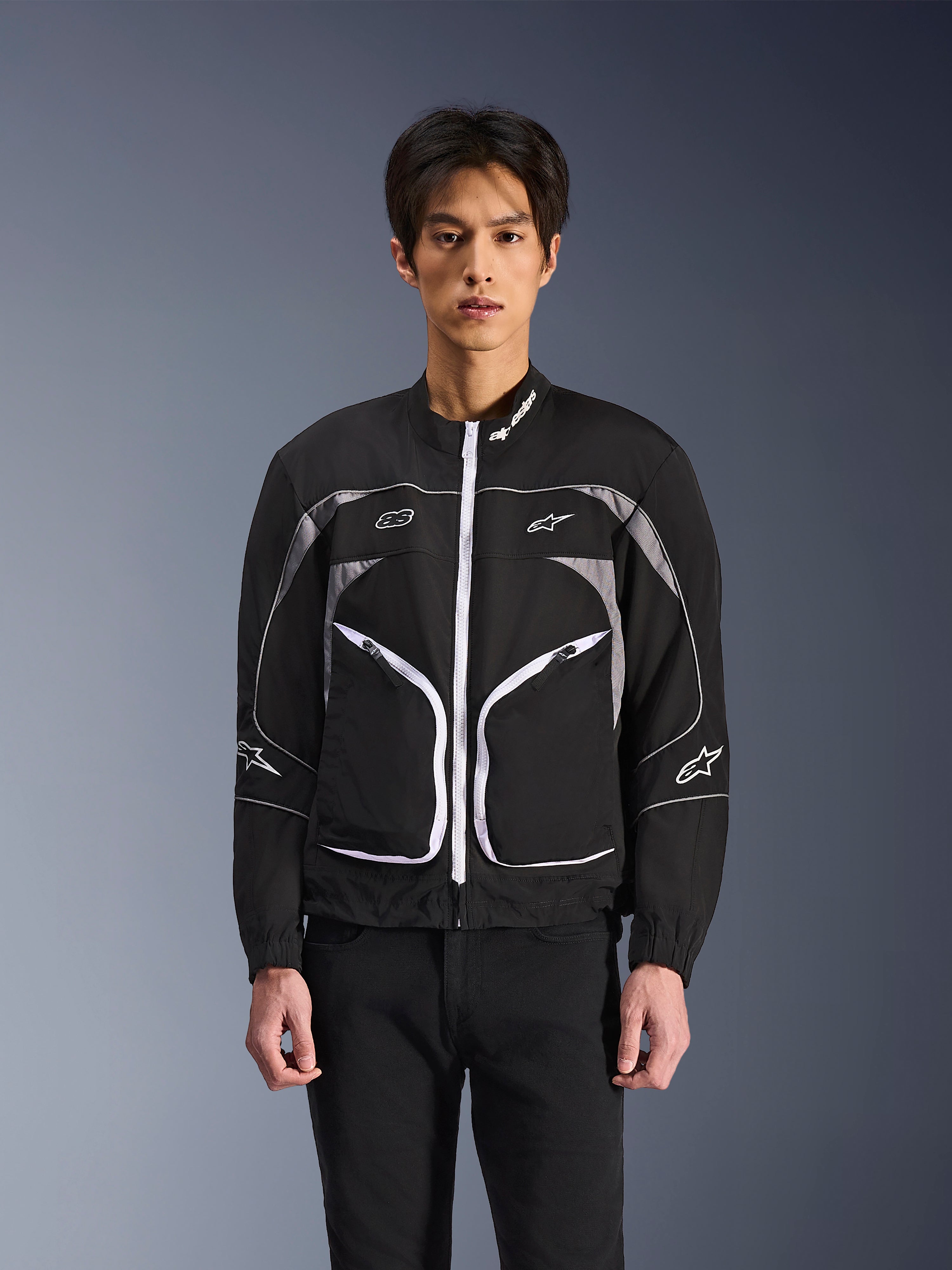 Alpinestars Unite-jakke, minimalistisk urban motorcykeljakke, sort og mørkegrå med hvide detaljer, hvid lynlås foran, reflekterende piping og Alpinestars-branding på brystet og ærmerne, moderne streetwear-stil til kørere.