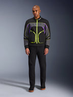 Mandlig model iført Alpinestars Unite-jakken i Black Asphalt Violet, med sort base, grå og lilla paneler og iøjnefaldende neongule lynlåse og detaljer, kombineret med sorte bukser og sko, minimalistisk urban motorcykeljakke.