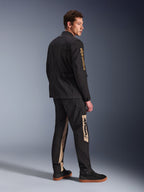 Alpinestars Dice-jakke, urban motorcykeljakke, sort, 3/4 bagfra set på model, vintage feltjakke-æstetik med guld Alpinestars-logo på ærmet, båret med matchende sorte og sandfarvede kørebukser og sorte sneakers