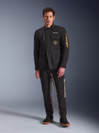 Mandlig model iført Alpinestars Dice Jacket, sort urban motorcykeljakke med vintage feltjakke-stil, fire funktionelle frontlommer, Alpinestars-branding på ærmet og brystet, kombineret med sorte og sandfarvede bukser, moderne urban køreudstyr