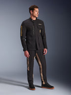 Mandlig model iført Alpinestars Dice-jakke i sort, urban motorcykeljakke med vintage feltjakke-æstetik, med flere funktionelle lommer og guld-branding på ærmet, kombineret med matchende sorte og sandfarvede bukser og sorte sneakers.