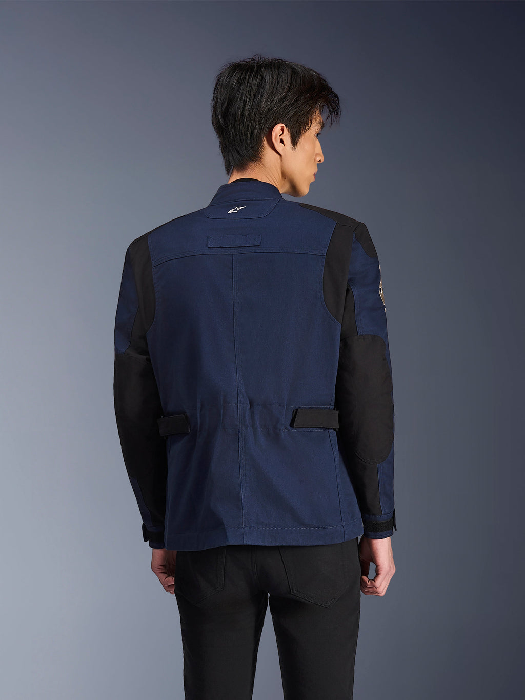 Alpinestars Dice Jacket, mørkeblå og sort urban field-motorcykeljakke, set bagfra båret af en mand, med forstærkede sorte skulder- og albuepaneler og justerbare stropper i taljen.