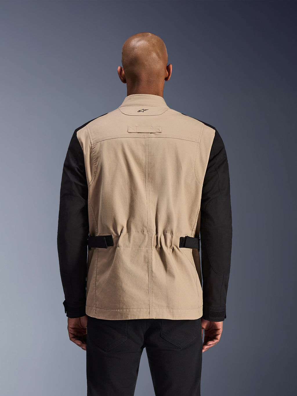 Alpinestars Dice-jakke, urban motorcykeljakke, Aluminum og sort, set bagfra på en model, med plisserede skuldre for mobilitet, justerbare taljeremme og en robust polybomulds-twill-konstruktion.