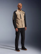 Alpinestars Dice-jakke, urban motorcykeljakke, Aluminum Black og tan, tofarvet design med sorte ærmer og khaki torso, båret af en model med sorte bukser og sorte sneakers, arbejdstøjsinspireret æstetik med funktionelle lommer og broderet branding på ærmet.