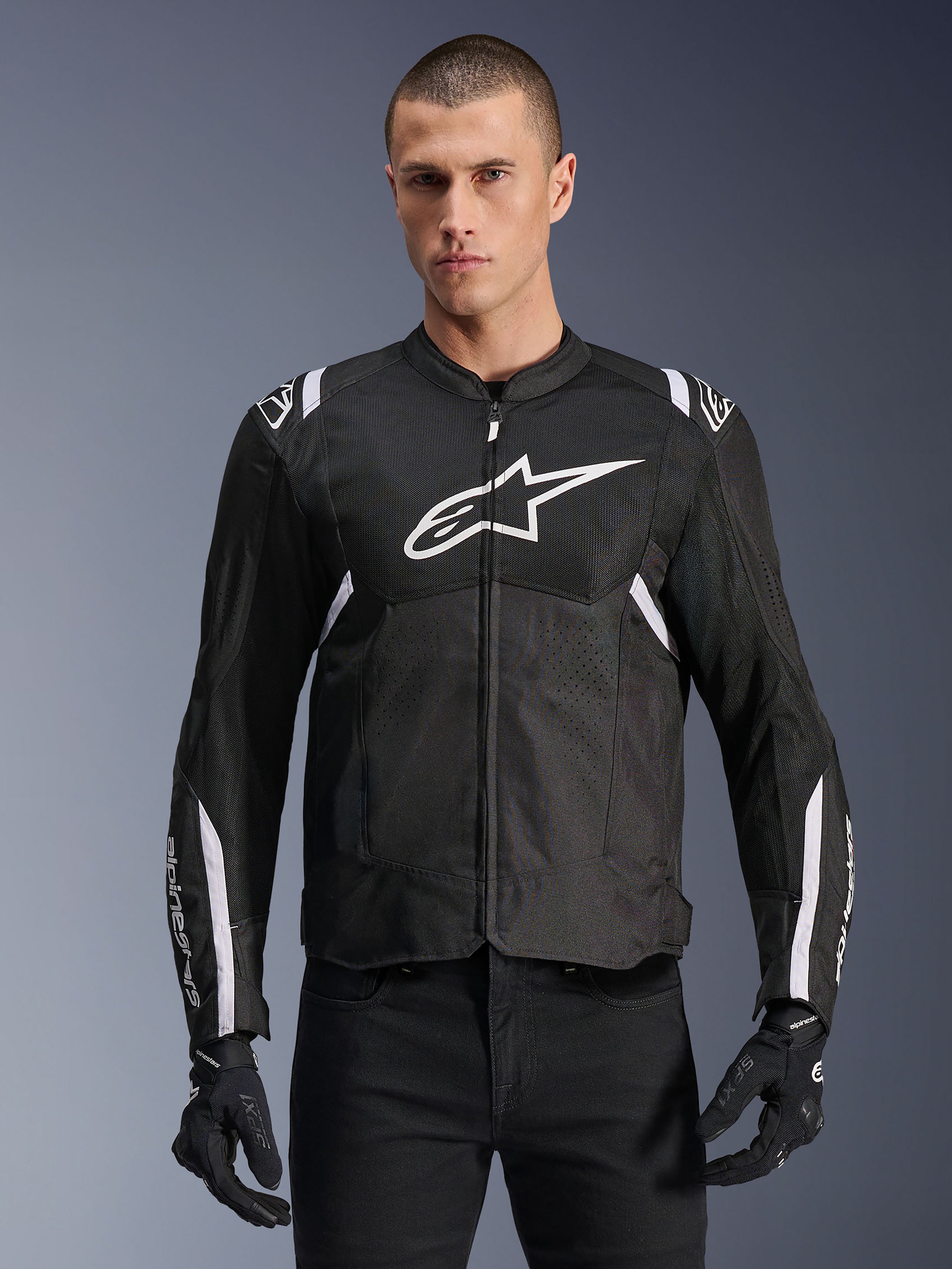 Alpinestars T-SPS Air V2 jakke, tekstil motorcykeljakke, sort med hvide detaljer, stort hvidt logo på brystet, perforeret mesh-design til ventilation, bæres med sorte bukser og handsker