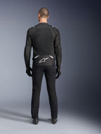 Alpinestars T-Sps Air V2 Jakke, set bagfra, sort og hvid tekstil motorcykeljakke, med et stort mesh-panel på ryggen for maksimal luftgennemstrømning og hvidt Astars-logo på den nederste del af ryggen, båret med sorte motorcykelbukser og handsker