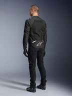 Alpinestars T-Sps Air V2 Jakke, tekstil motorcykeljakke, sort, set bagfra med et stort mesh-ventilationspanel og hvidt Alpinestars-logo nederst på ryggen, kombineret med sorte kørebukser og handsker for et sporty urbant look.