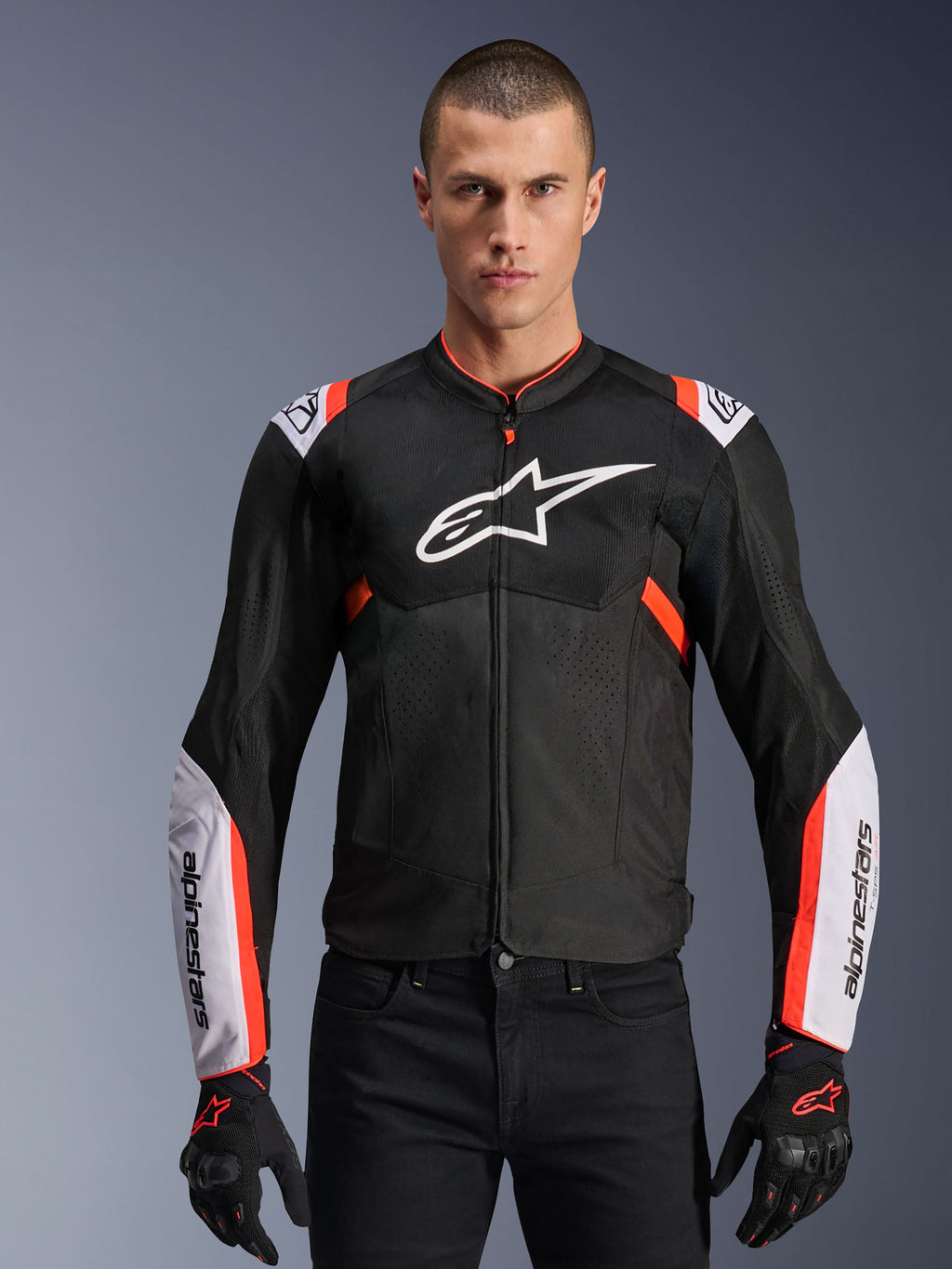 Alpinestars T-Sps Air V2-jakke, sort med hvide og rød fluo-detaljer, motorcykel-sportsjakke, mand iført et mesh-ventileret design med stort logo på brystet og brandede ærmer, kombineret med sorte handsker og bukser