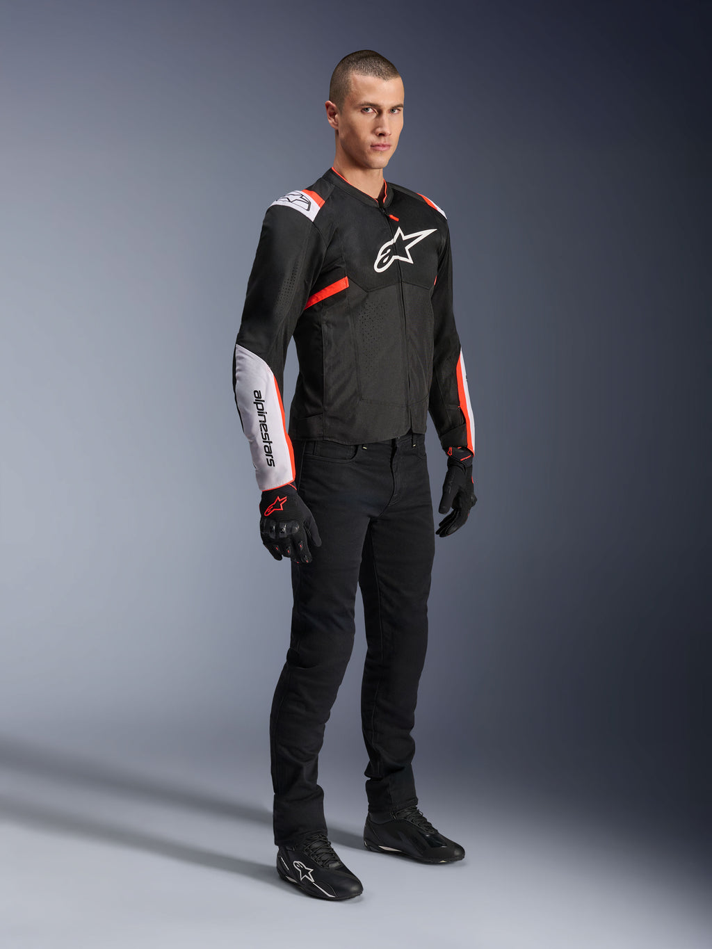 Alpinestars T-Sps Air V2 jakke, sort, hvid og rød fluo, båret af en mandlig model med sorte køre-bukser og handsker, tekstil motorcykeljakke med store mesh-paneler, hvide skulder- og underarmssektioner og et markant Alpinestars-logo på brystet