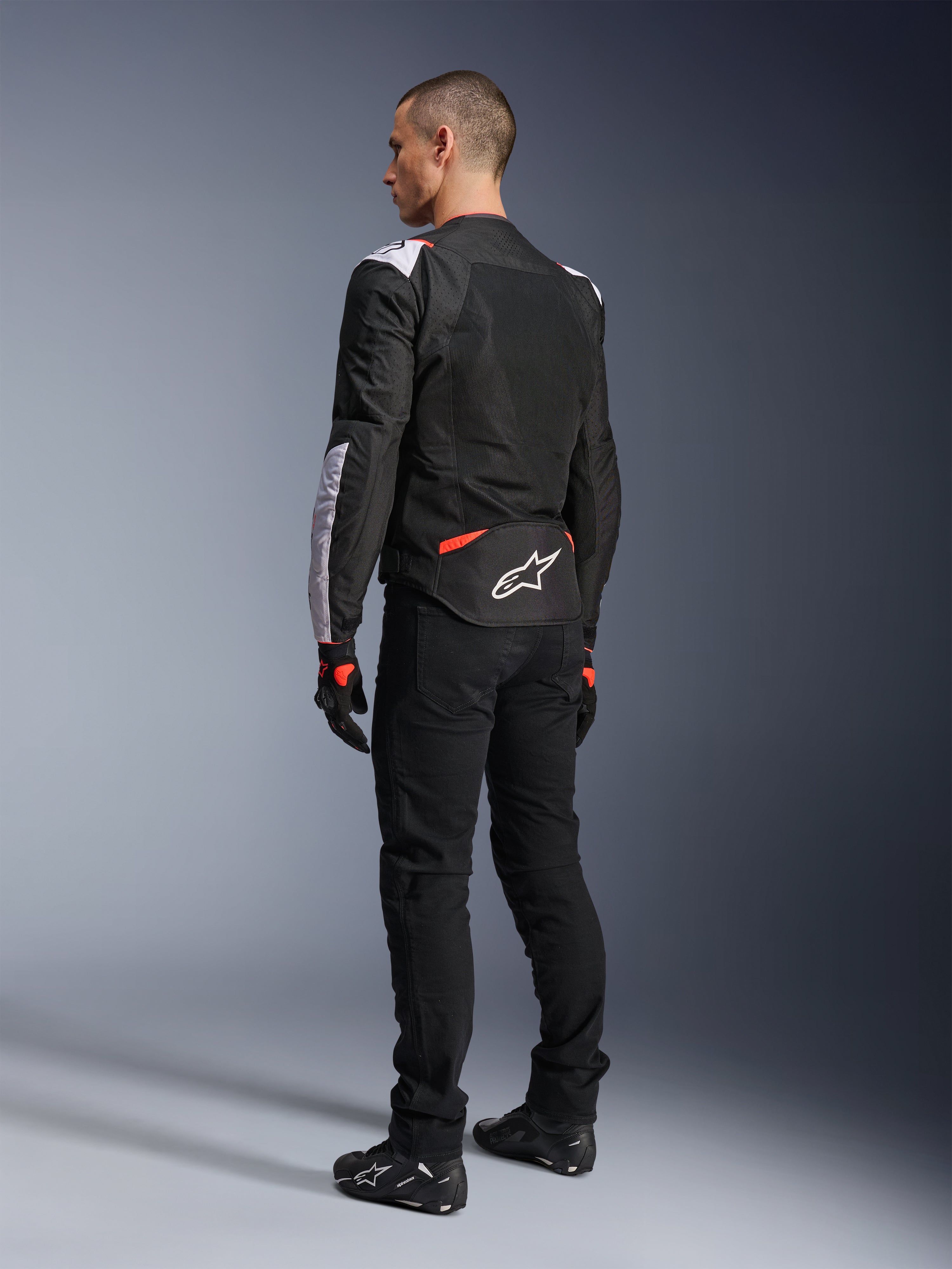 Alpinestars T-Sps Air V2-jakke, tekstilmotorcykeljakke, sort, hvid og rød fluo, set bagfra på model, mesh-paneler til ventilation, hvidt Astars-logo på den nedre del af ryggen, stylet med sorte kørebukser og handsker