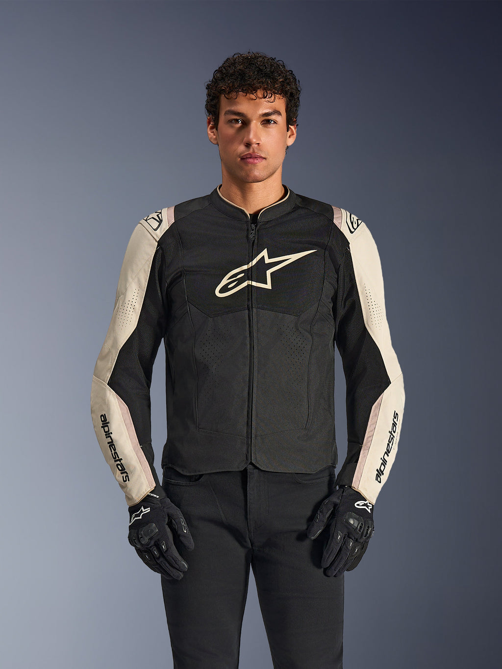 Alpinestars T-SPS Air V2 jakke, motorcykeljakke, sort og mastic aluminum, mandlig model iført jakke med sorte bukser og handsker, med mesh-paneler til ventilation, stort Alpinestars-logo på brystet og sporty, tætsiddende design
