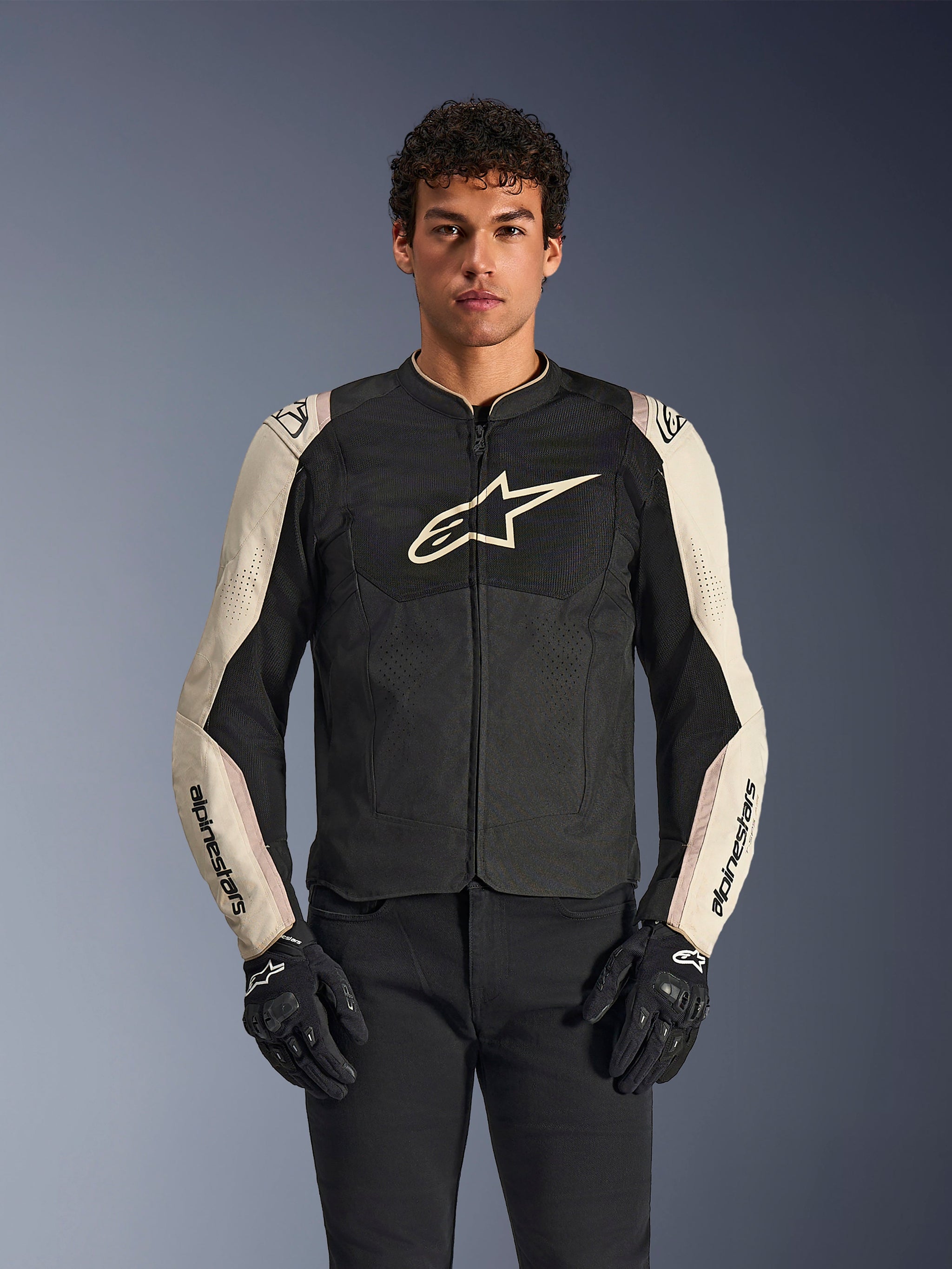 Alpinestars T-SPS Air V2-jakke i Black Mastic Aluminum, tekstil motorcykeljakke med ventilerede mesh-paneler, lysegrå ærmer med sort Alpinestars-skrift, stort hvidt stjernelogo på brystet, båret med sorte bukser og handsker.
