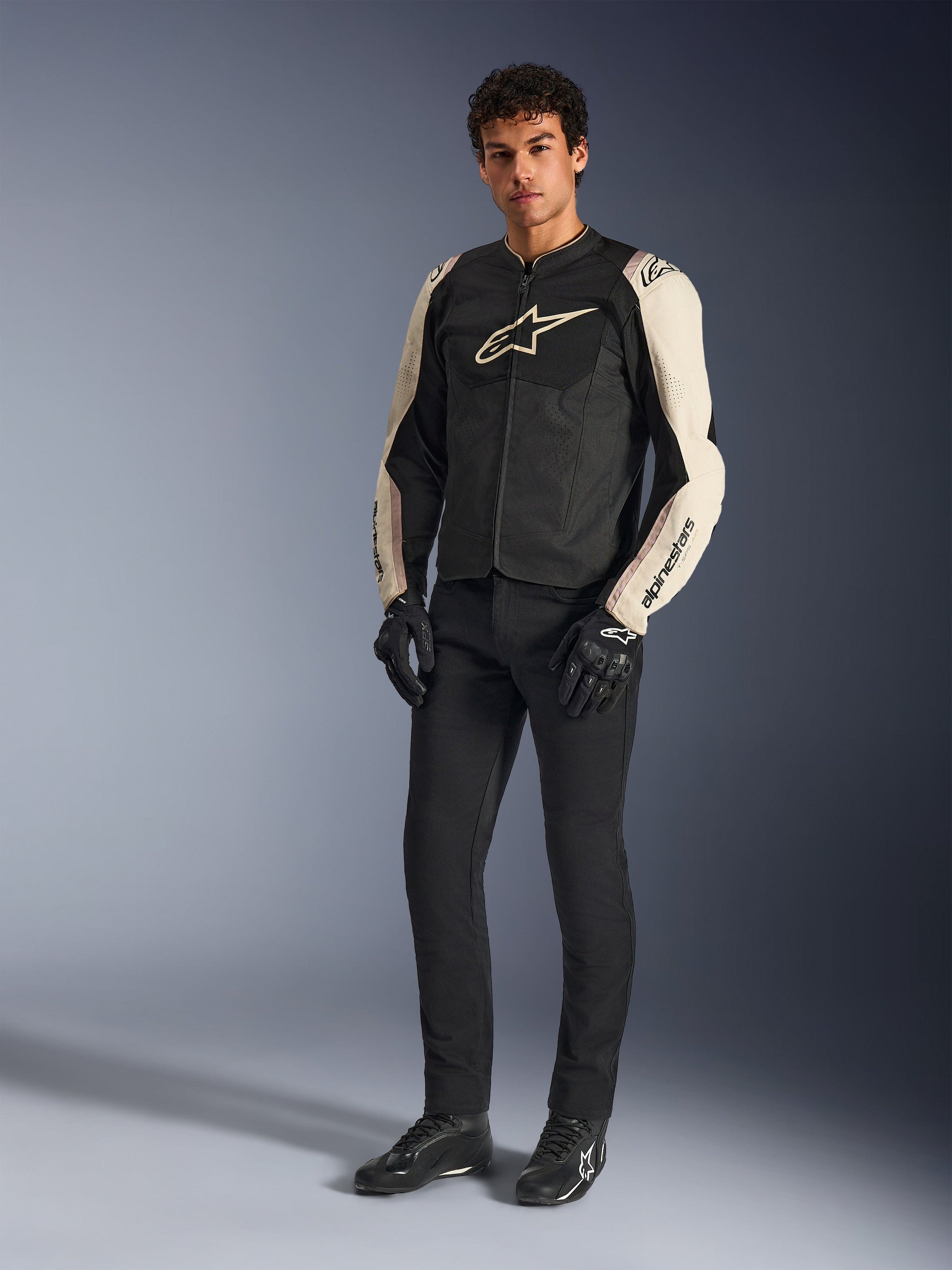 Alpinestars T-SPS Air V2 jakke, Black Mastic Aluminum, båret af en model med sorte kørebukser og handsker, ventileret tekstil-motorcykeljakke med mesh-paneler og sporty design, studieoptagelse i fuld figur.