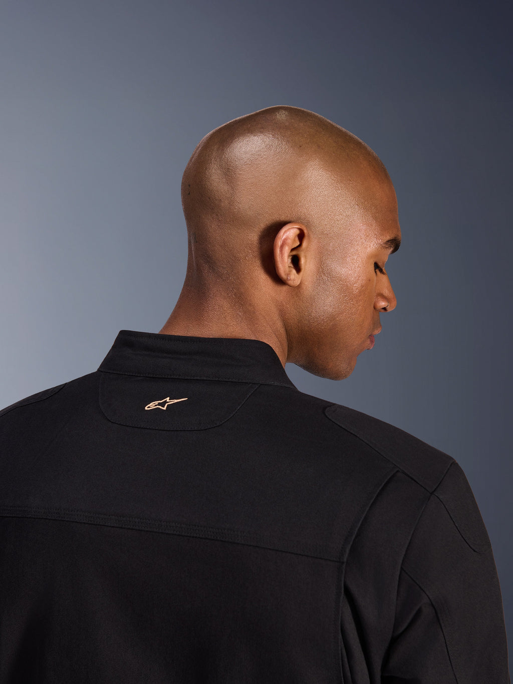 Alpinestars Bruiser Jakke, sort, detaljebillede bagfra af kraven og de øverste skuldre, med et lille sandfarvet broderet Alpinestars-logo på nakken, urban motorcykeljakke med arbejdstøjsæstetik